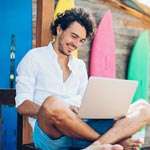 Small business owner sits cross-legged outside his surf shop and accesses FreeConferenceCall.com free recordings on his laptop