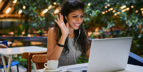 Image of a woman waving at her computer outside with headphones in